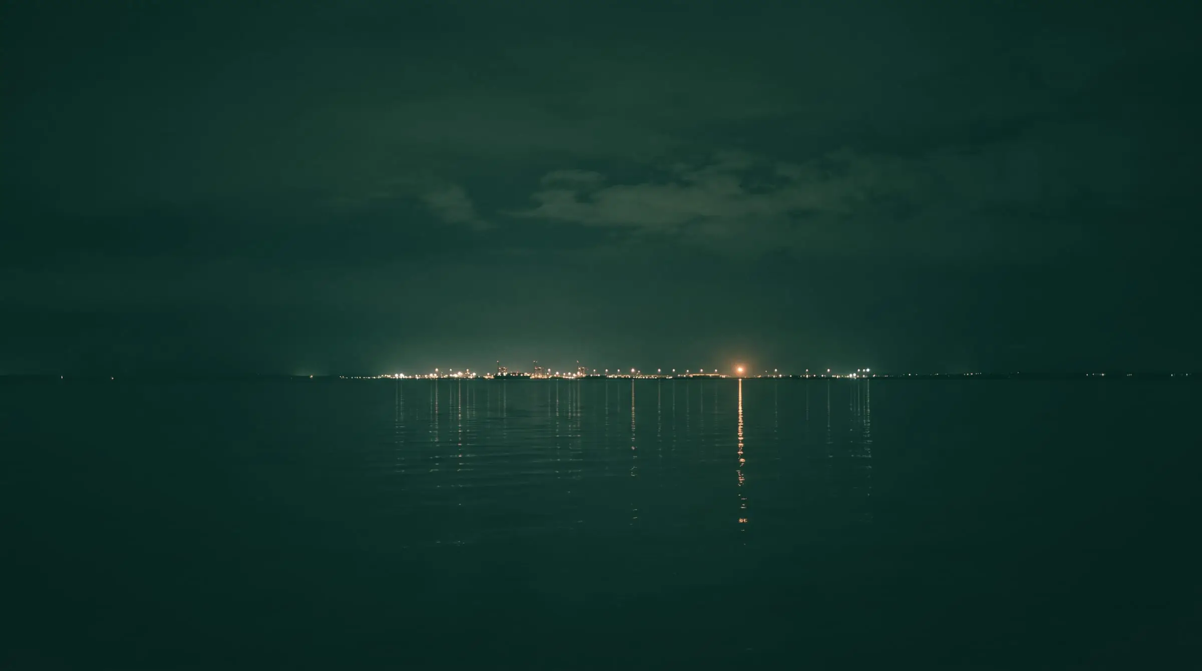 A port seen across dark water at night, its lights reflected in long streaks.